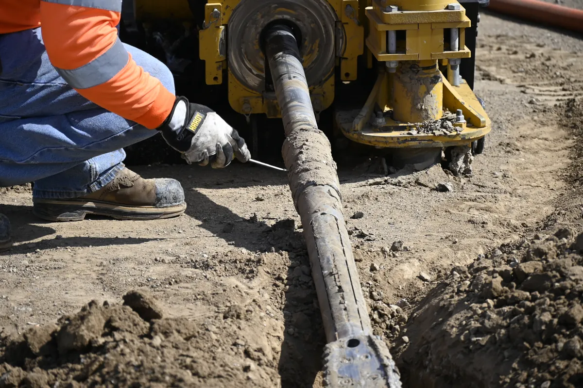Worker inspecting transmitter-housing tooling beside an HDD drill rig.